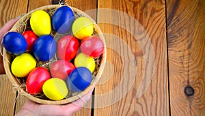 Female hands hold a plate with colorful easter eggs over a wooden table