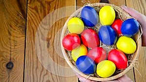 Female hands hold a plate with colorful easter eggs over a wooden table