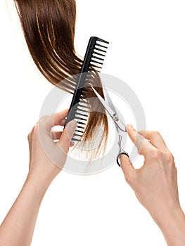 Female hands hold professional hairdressing tools, comb and scissors next to brown hair