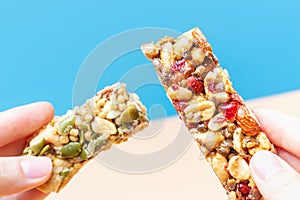 Female hands hold a protein bars on blue and brown background.