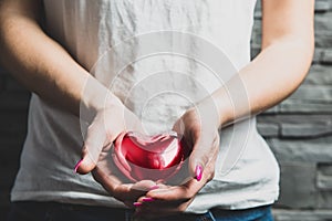 Female hands hold a red metal heart