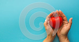 female hands hold a red toy heart on a blue background, health care, life insurance, women's health, mothe