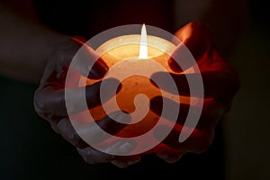 Female hands hold a round white candle with a burning flame