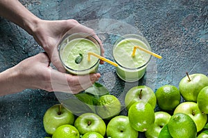 Female hands hold smoothies apples and limes on a dark blue concrete background. Detox programm