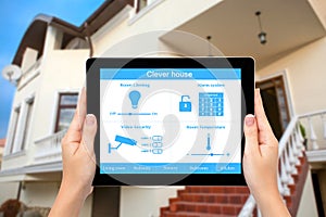 Female hands hold a tablet with system clever house on the background of the house