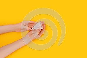 Female hands hold white menstrual cup on a bright yellow background.