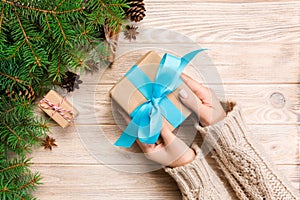 Female hands hold wrapping christmas gift box with blue ribbon on brown wooden table. Top view