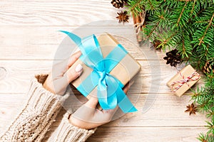female hands hold wrapping christmas gift box with blue ribbon on brown wooden table. Top view