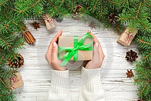 Female hands hold wrapping christmas gift box with green ribbon on white wooden table. Top view