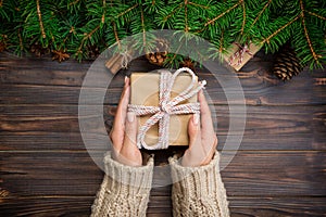 Female hands hold wrapping christmas gift box with pink ribbon on dark wooden table. Top view