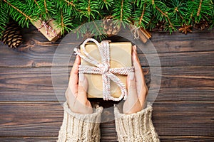 female hands hold wrapping christmas gift box with pink ribbon on dark wooden table. Top view