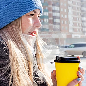 female hands hold a yellow paper cup with coffee, hands sip hot coffee. coffee to go warm in cold weather