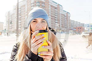 female hands hold a yellow paper cup with coffee, hands sip hot coffee. coffee to go warm in cold weather