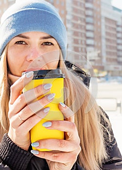 female hands hold a yellow paper cup with coffee, hands sip hot coffee. coffee to go warm in cold weather.