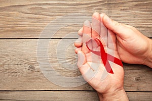 A female hands holding an aids red ribbon on grey