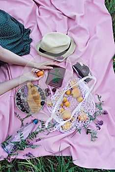 Female hands holding apricot fruit on a pink blanket on a grass