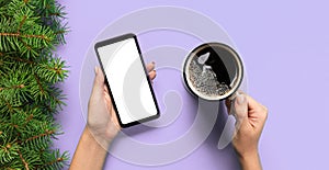 Female hands holding black mobile phone with blank white screen and mug of coffee. Mockup banner image with copy space. Top view