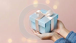 Female hands holding blue beautiful gift box on pink background with copy space