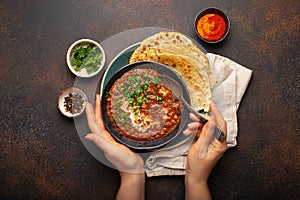 Female hands holding a bowl and eating traditional Indian Punjabi dish Dal makhani with lentils and beans served with