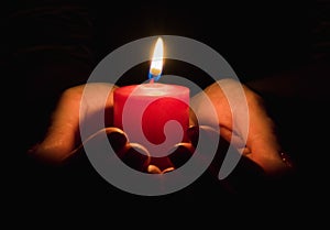 Female hands holding a burning candle in the dark