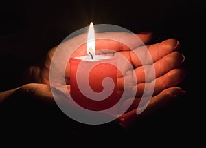 Female hands holding a burning candle in the dark