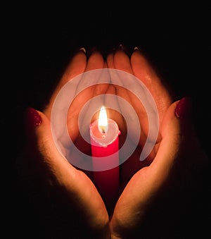 Female hands holding a burning candle in the darkness, hugging it around