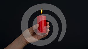 Female hands holding a burning red candle on dark background