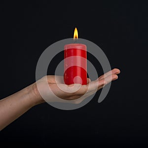 Female hands holding a burning red candle on dark background