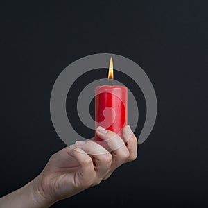 Female hands holding a burning red candle on dark background