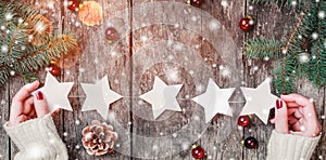 Female hands holding Christmas garland of stars on wooden background with Christmas gifts, Fir branches, red decorations.
