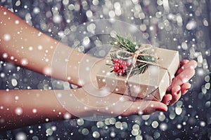 Female hands holding Christmas gift box with branch of fir tree, shiny xmas background