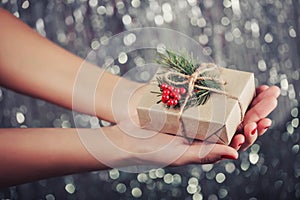 Female hands holding Christmas gift box with branch of fir tree, shiny xmas background.
