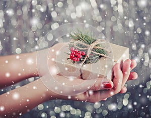 Female hands holding Christmas gift box with branch of fir tree, shiny xmas background.