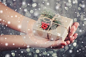 Female hands holding Christmas gift box with branch of fir tree, shiny xmas background.