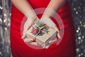 Female hands holding Christmas gift box with branch of fir tree, shiny xmas background.