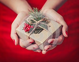 Female hands holding Christmas gift box with branch of fir tree, shiny xmas background. Holiday gift and decoration