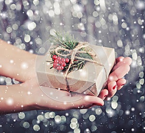 Female hands holding Christmas gift box with branch of fir tree, shiny xmas background. Holiday gift and decoration