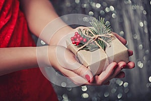 Female hands holding Christmas gift box with branch of fir tree, shiny xmas background. Holiday gift and decoration