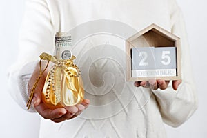 Female hands holding Christmas gift box with dollar and calendar, xmas. 25 Desember. background. Holiday gift and decoration