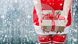 Female hands holding Christmas gift box with red ribbon, branch of fir tree on shiny xmas background.