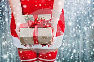 Female hands holding Christmas gift box with red ribbon, branch of fir tree on shiny xmas background. Holiday gift