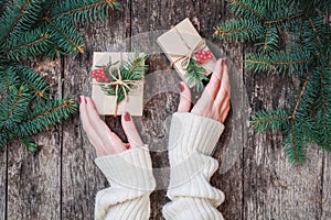 Female hands holding Christmas gifts with Fir branches on wooden background. Xmas and Happy New Year composition