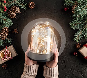 Female hands holding Christmas glowing ball on holiday background with Fir branches, gifts. Xmas and Happy New Year card, bokeh,