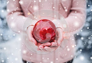 Female hands holding a Christmas red ball. Frosty winter day in snowy forest.