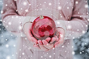 Female hands holding a Christmas red ball. Frosty winter day in snowy forest.