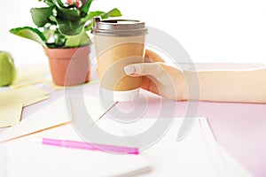 The female hands holding coffee on trendy pink desk.