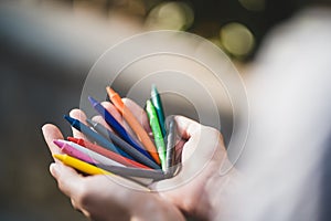 Female hands holding colorful pencils in the park. Bunch of multicolored crayons in hand