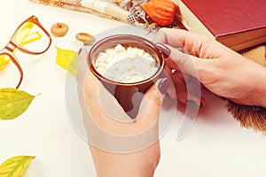 Female hands holding cup of cacao. Autumn table with leaves, book, glasses and coffee. Autumn mood. Mockup