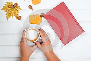 Female hands holding a cup of cappuccino. Autumn background.