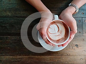 Female hands holding cup of chocolate on wooden background. top vie